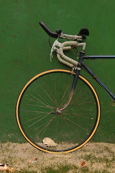 Close-up of a vintage racing bicycle wheel leaning on a textured green wall.
